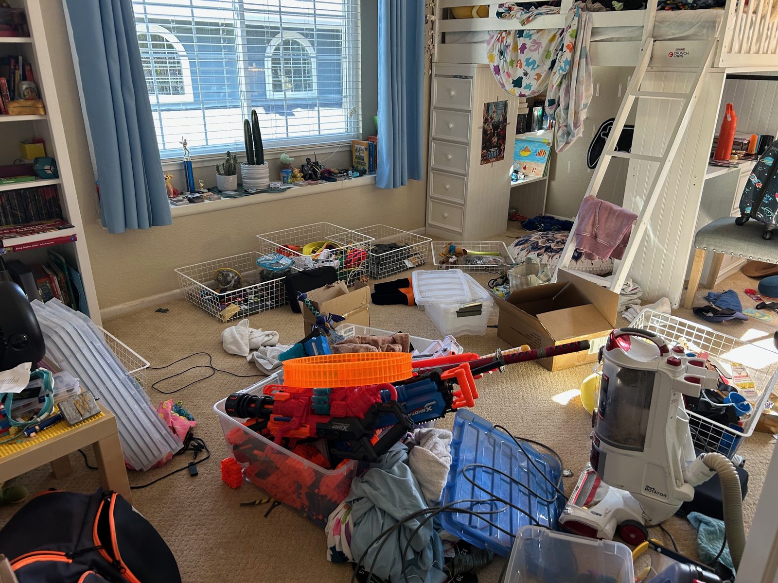 Kids' bedroom before — toys, bins, and boxes covering the floor beneath the loft bed